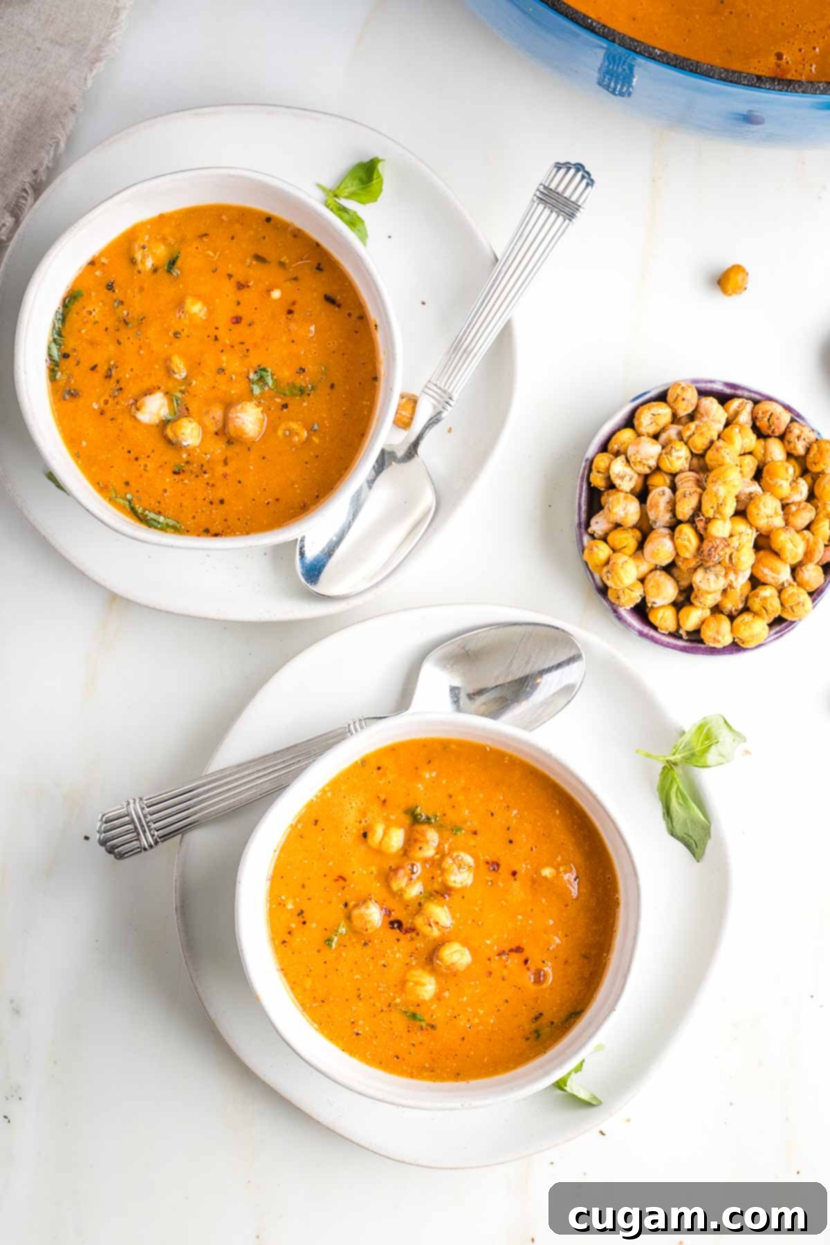 Creamy Dairy-Free Tomato Soup Recipe 13 Two bowls of creamy dairy-free tomato soup, beautifully garnished, with a separate bowl of crunchy chickpeas for topping.