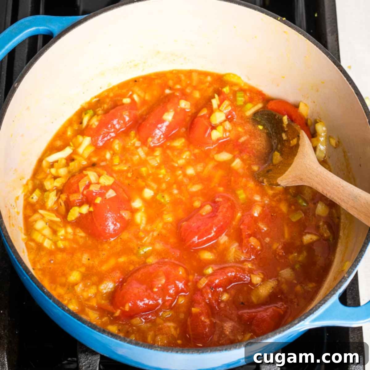 Creamy Dairy-Free Tomato Soup Recipe 8 Squishing whole tomatoes with the back of a wooden spoon in a Dutch oven to break them down for soup.