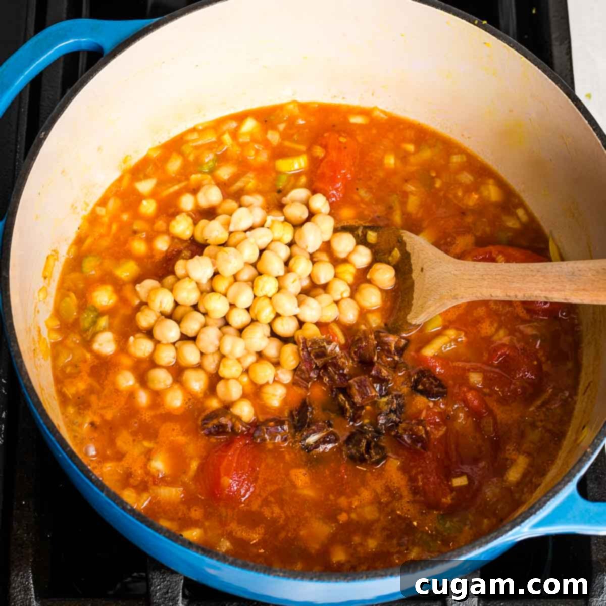 Creamy Dairy-Free Tomato Soup Recipe 9 Tomato-based soup with chickpeas and chopped dates added on top, simmering in a Dutch oven.