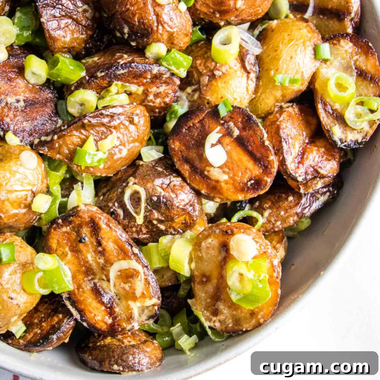 Close up quarter of a white bowl loaded with grilled potato salad with fresh scallions and a creamy mustard dressing, ready to be served.