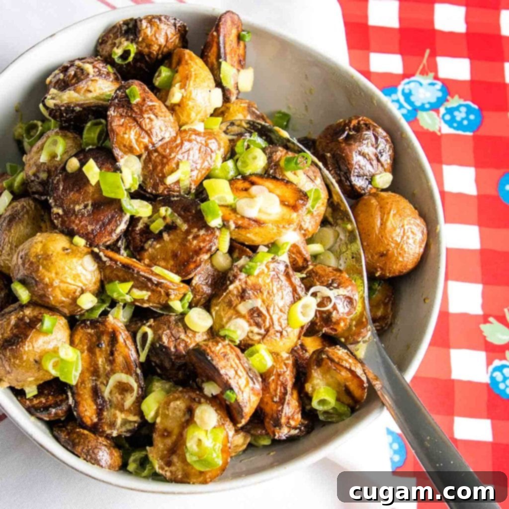 White bowl filled with delicious grilled potatoes, coated in a creamy mustard sauce and garnished with fresh scallions, set against a vibrant red checkered background.