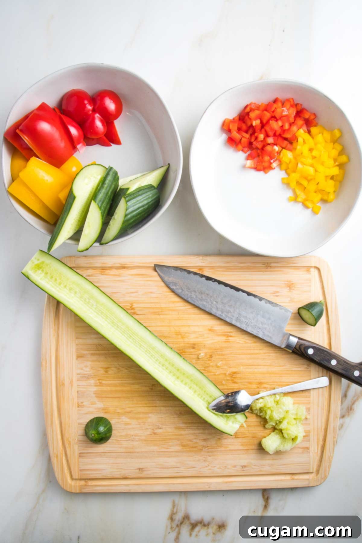 cutting board with english cucumber halved lengthwise and then seeds scooped out. Plus two white bowls with chunks of red and yellow peppers or diced smaller red and yellow peppers. 