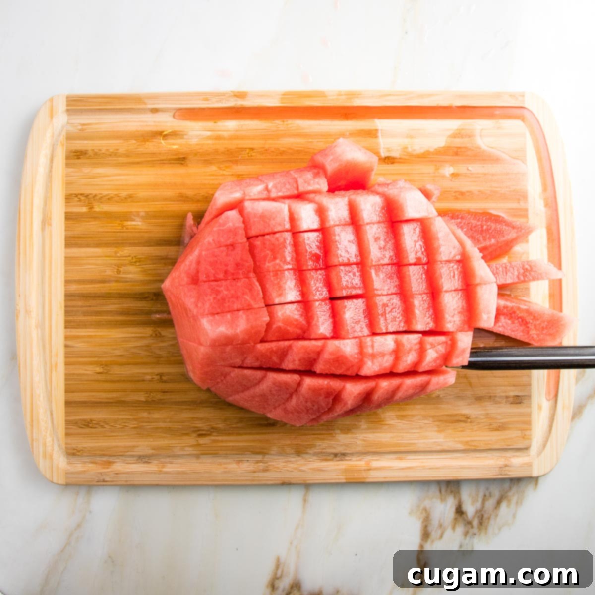 wooden board showing how to cube watermelon and the groove on the board is catching the watermelon juice.
