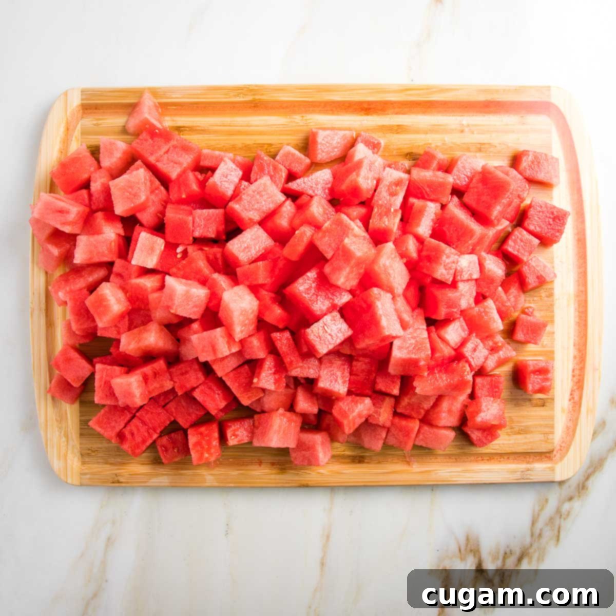 wooden cutting board with chunks of watermelon, and watermelon juice accumulated in the board groove.