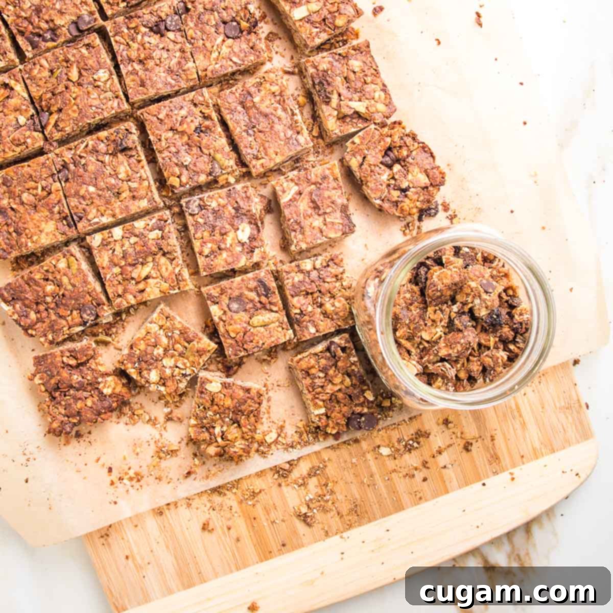 granola bars cut into squares, lots of crumbs and a glass container holding the granola crumbs.