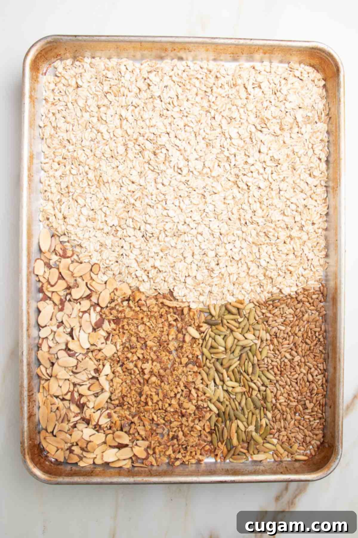 Large rimmed baking tray with oats, sliced almonds, chopped walnuts, sesame seeds and pumpkin seeds