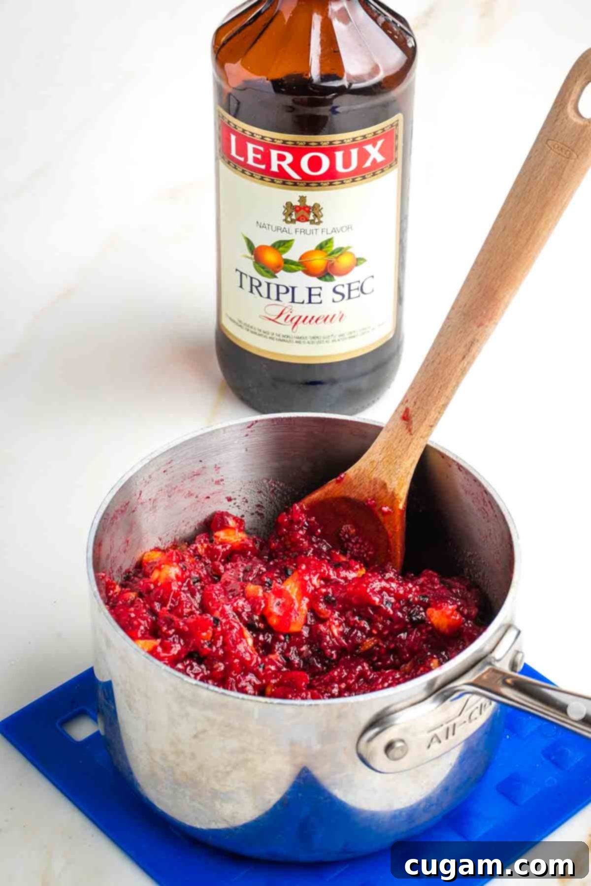 Stirring triple sec into a pot of fresh cranberry sauce.