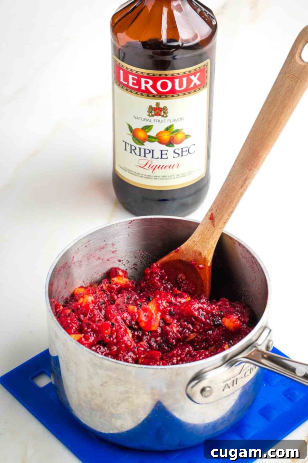 Stirring triple sec into a pot of fresh cranberry sauce.