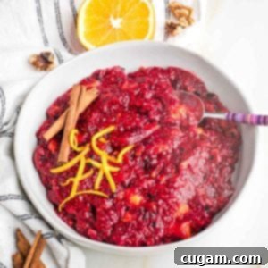 Bowl of chunky cranberry sauce with orange peel and cinnamon sticks.