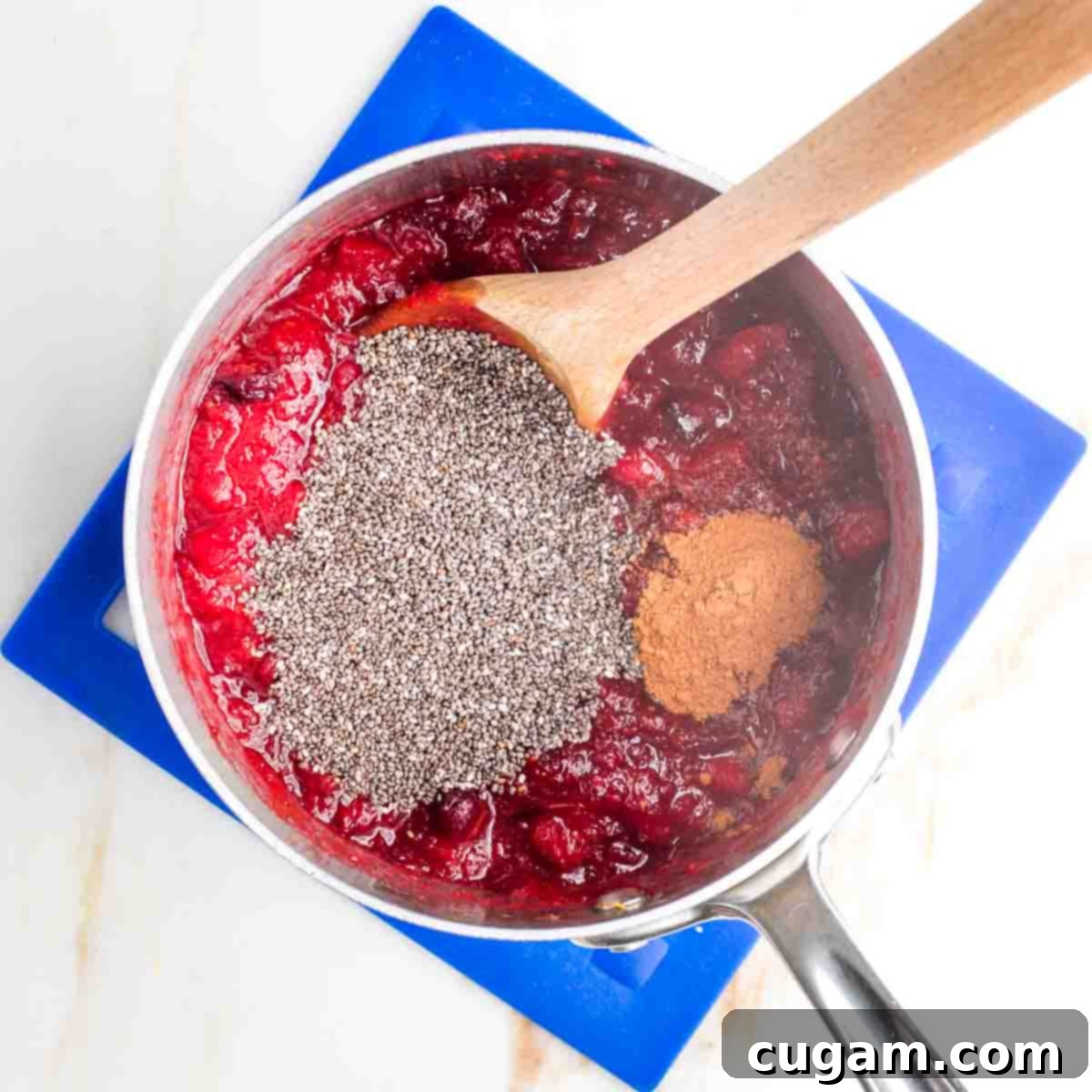 Chia seeds and cinnamon added to a small pot with cooked cranberries and oranges.