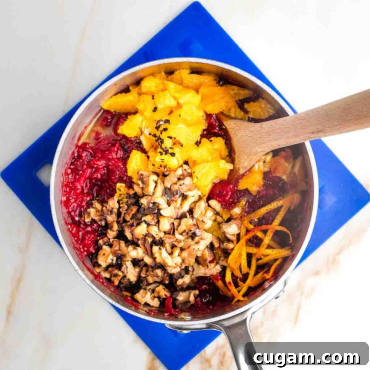 Cooked cranberries in a small pot with chopped oranges, orange zest and toasted walnuts.