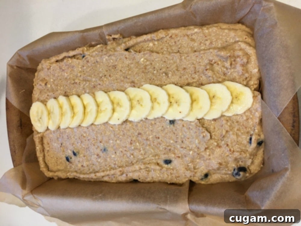 A loaf pan filled with banana bread batter, elegantly topped with a row of thinly sliced bananas, ready for baking.