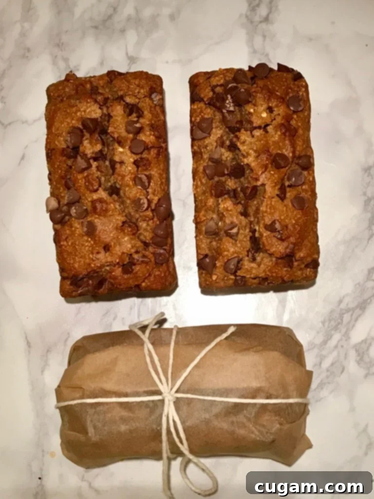 Several mini loaves of chocolate chip banana bread. One is beautifully wrapped in unbleached parchment paper and tied with rustic kitchen twine, showcasing it as a perfect gift.