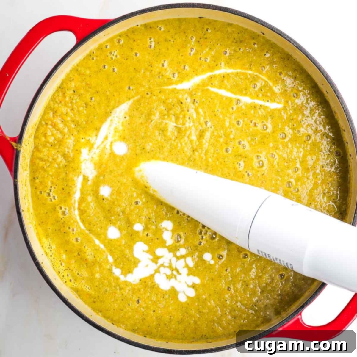 Immersion blender pureeing soup with a streak of white cream throughout.