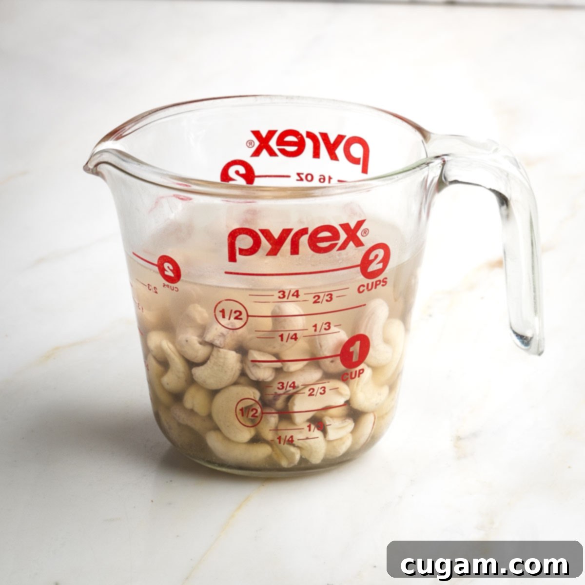 Pyrex measuring cup with cashews immersed in water.