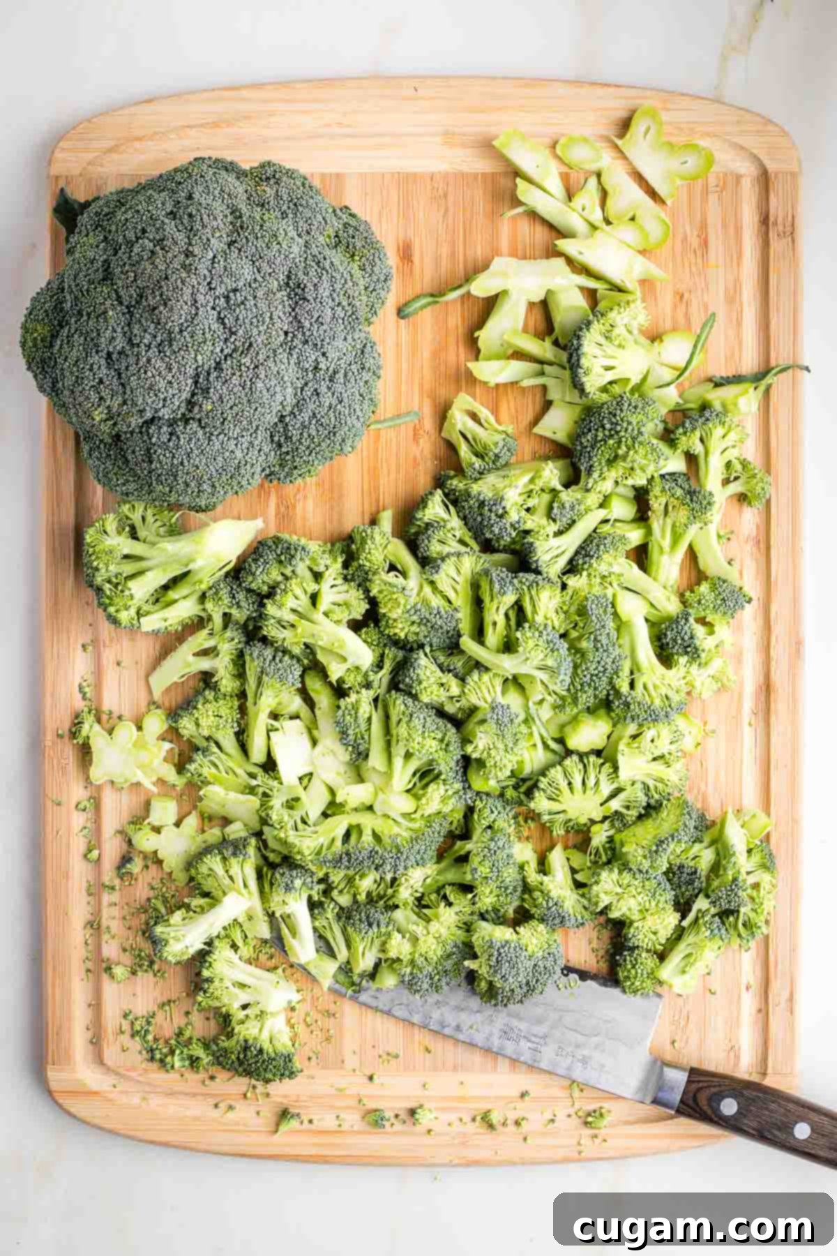 Head of broccoli, plus another crown that's been trimmed on a wood cutting board.