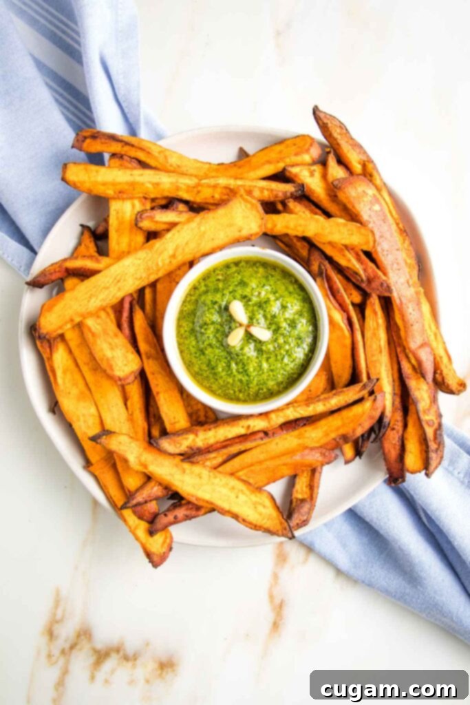 Large plate of crispy sweet potato fries with a small dish of bright green pesto in the center. 