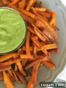 Crispy sweet potato fries on a grey plate with a dish of avocado dressing in the center.