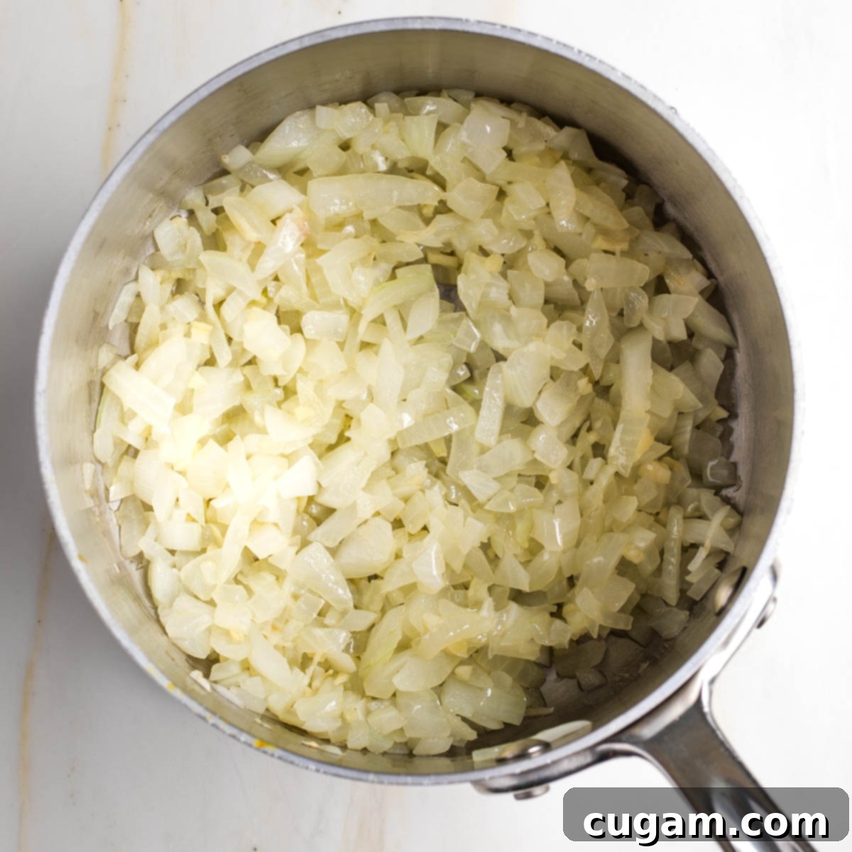 Diced onions being sautéed until translucent in a small saucepan, with a wooden spoon stirring them.