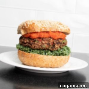 Veggie burger with red sauce, lettuce and a sesame bun on a plate.