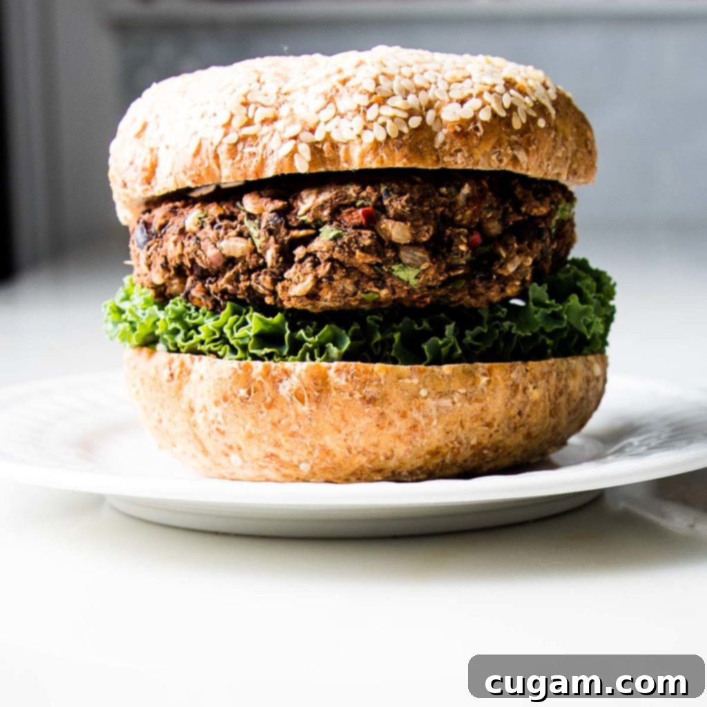 White plate with a burger in sesame seed bun on top of lettuce.