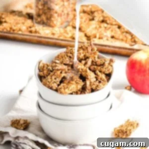 Pouring milk onto a bowl of granola with a tray of granola in the background and crumbs all around, plus a red apple.