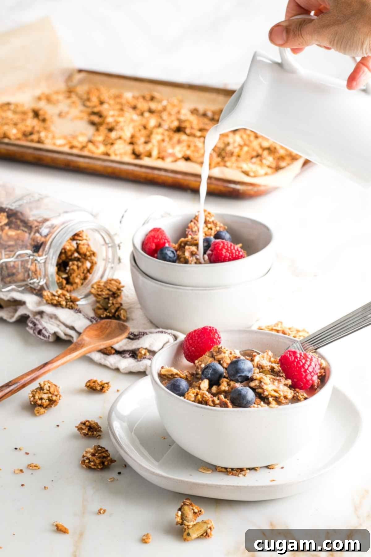 Bowls of granola with a tray in the background. Almond milk pouring into one of the bowls.