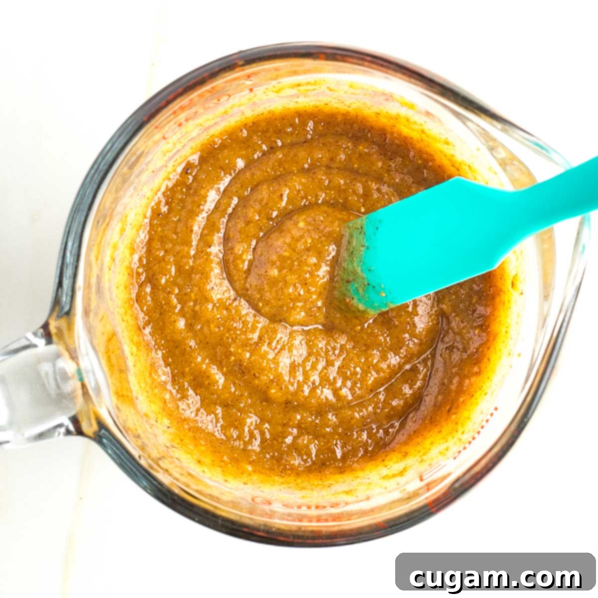 Thick brown pasty mixture in a pyrex measuring cup with bright blue spatula, representing the wet ingredients.