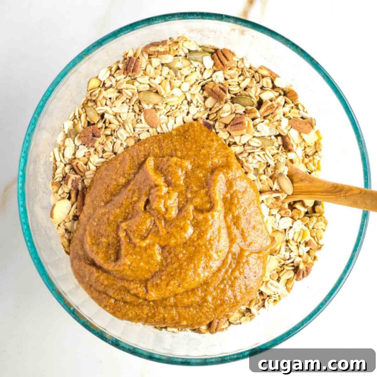 Mixture of oats and nuts in a large bowl with a mixture of almond butter plus applesauce and syrup poured over it.