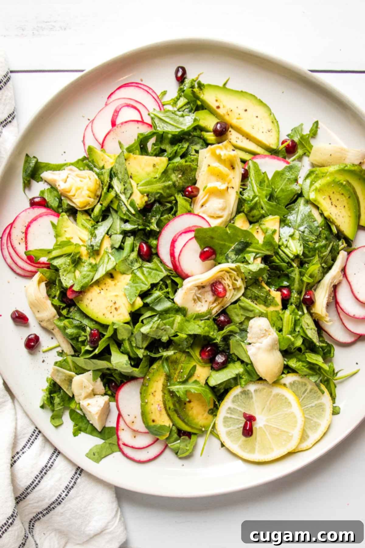 Arugula salad with artichoke hearts, avocado radish and lemon slices, beautifully arranged in a large white bowl.