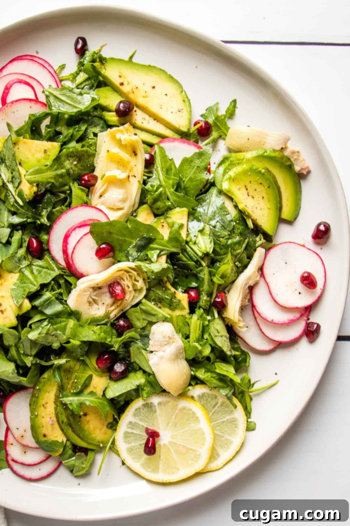 Composed salad with fresh arugula, creamy avocado, tender artichoke hearts, and thinly sliced radishes, with a scattering of vibrant pomegranate seeds for garnish.