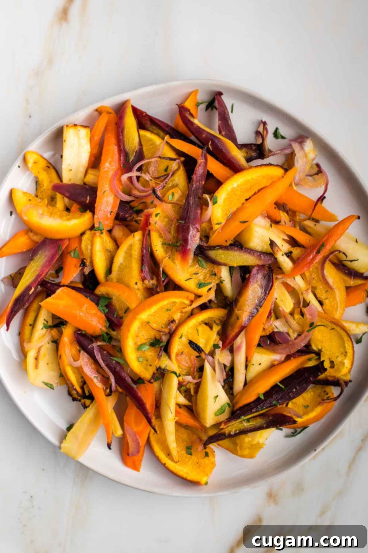 Brightly colored roasted root vegetables, purple and orange carrots, onions, parsnips and oranges. 