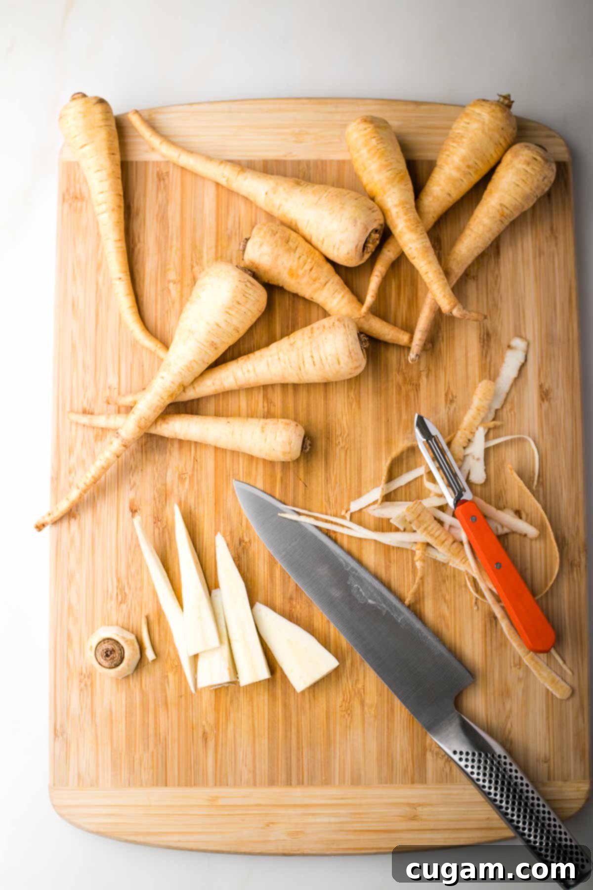 Fresh parsnips on a cutting board. One is peeled and sliced lengthwise.