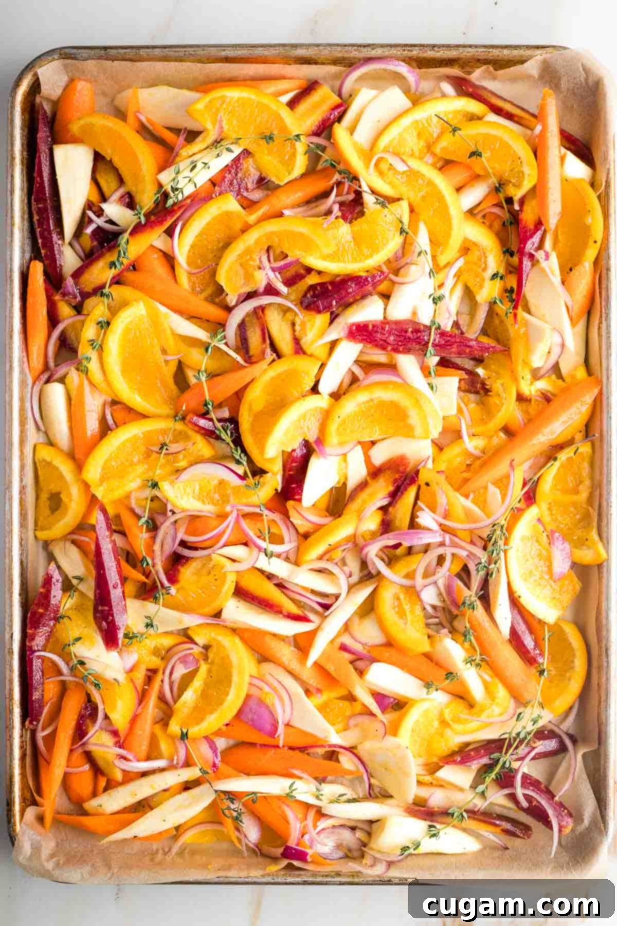 Parsnips, carrots, oranges and onions in a honey glaze on a baking tray.