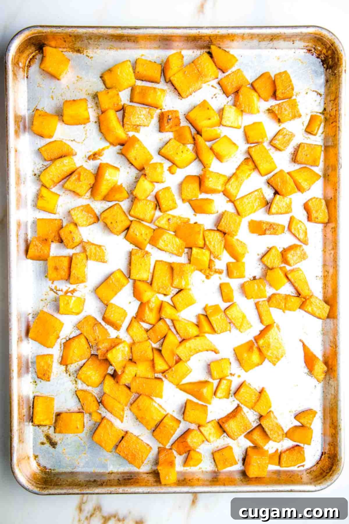 Roasted butternut squash cubes on a large rimmed baking sheet.