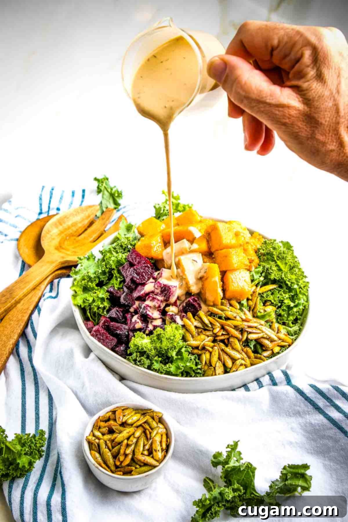 Pouring creamy dressing on top of roasted Butternut Squash and Beetroot cubes with kale.