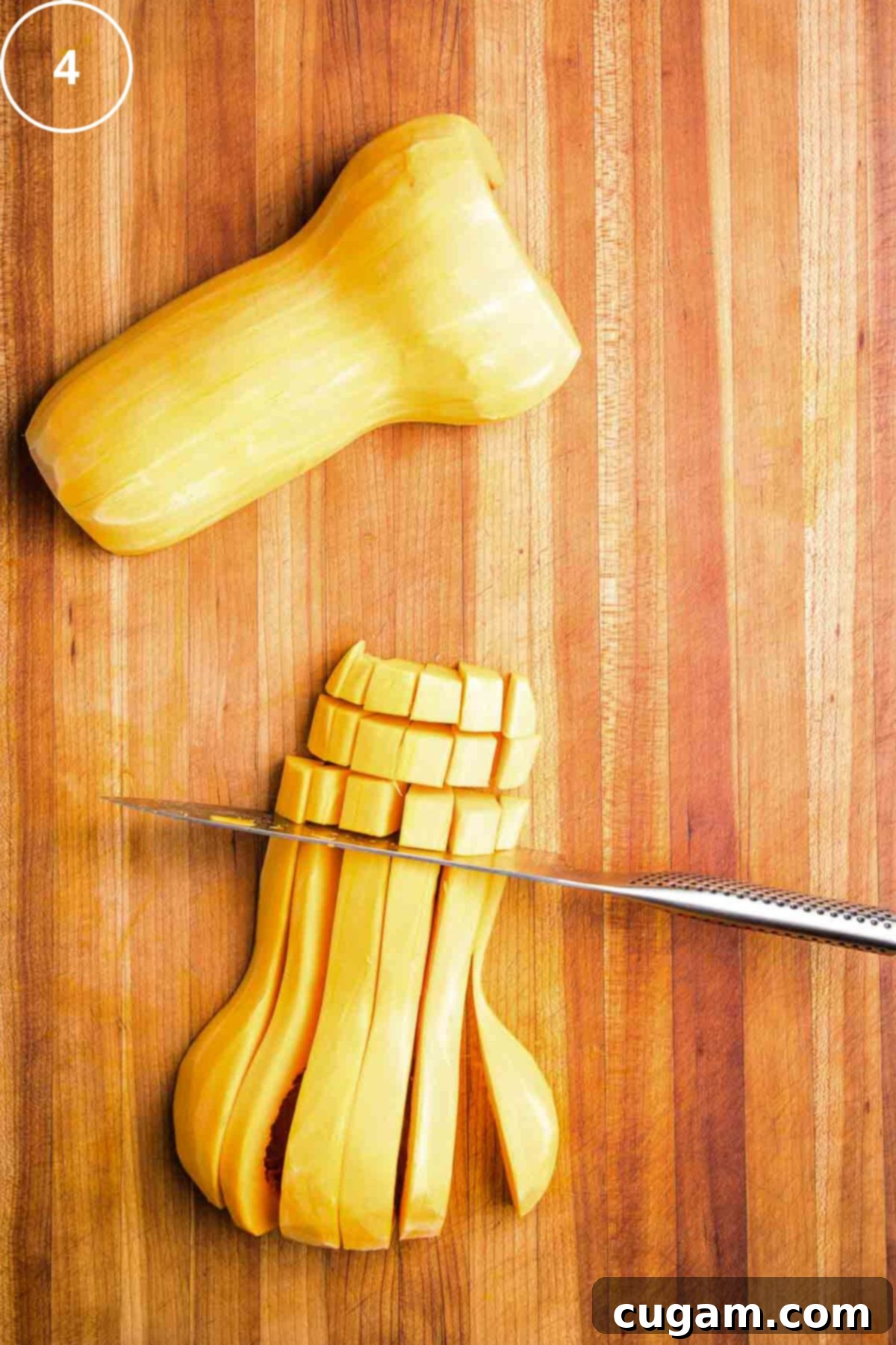 Chef's knife cutting through long strips of butternut squash to create ½ inch cubes.