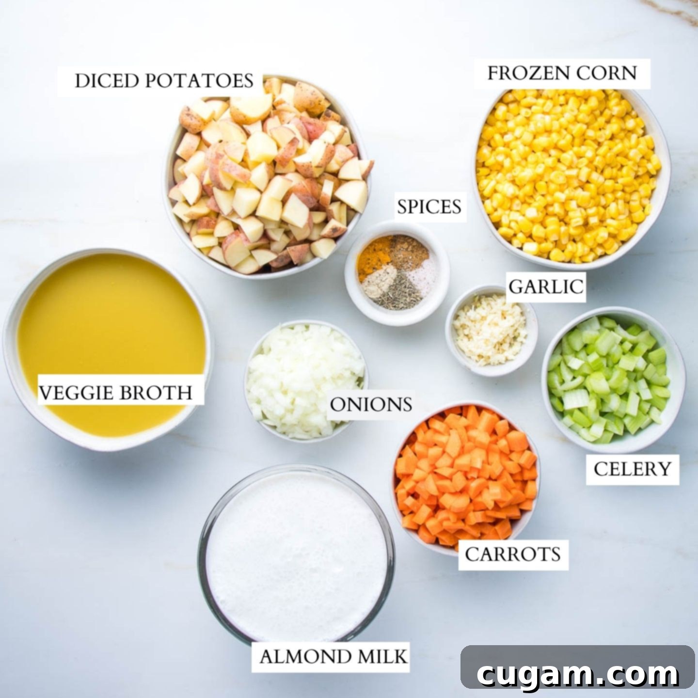 Labeled ingredients in bowls for corn chowder: diced potatoes, frozen corn, spices, minced garlic, onions, veggie broth, almond milk, carrots, celery. 