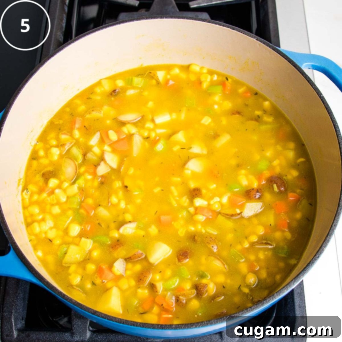 A dutch oven with yellow broth with corn, potatoes, carrots and celery floating in it. 