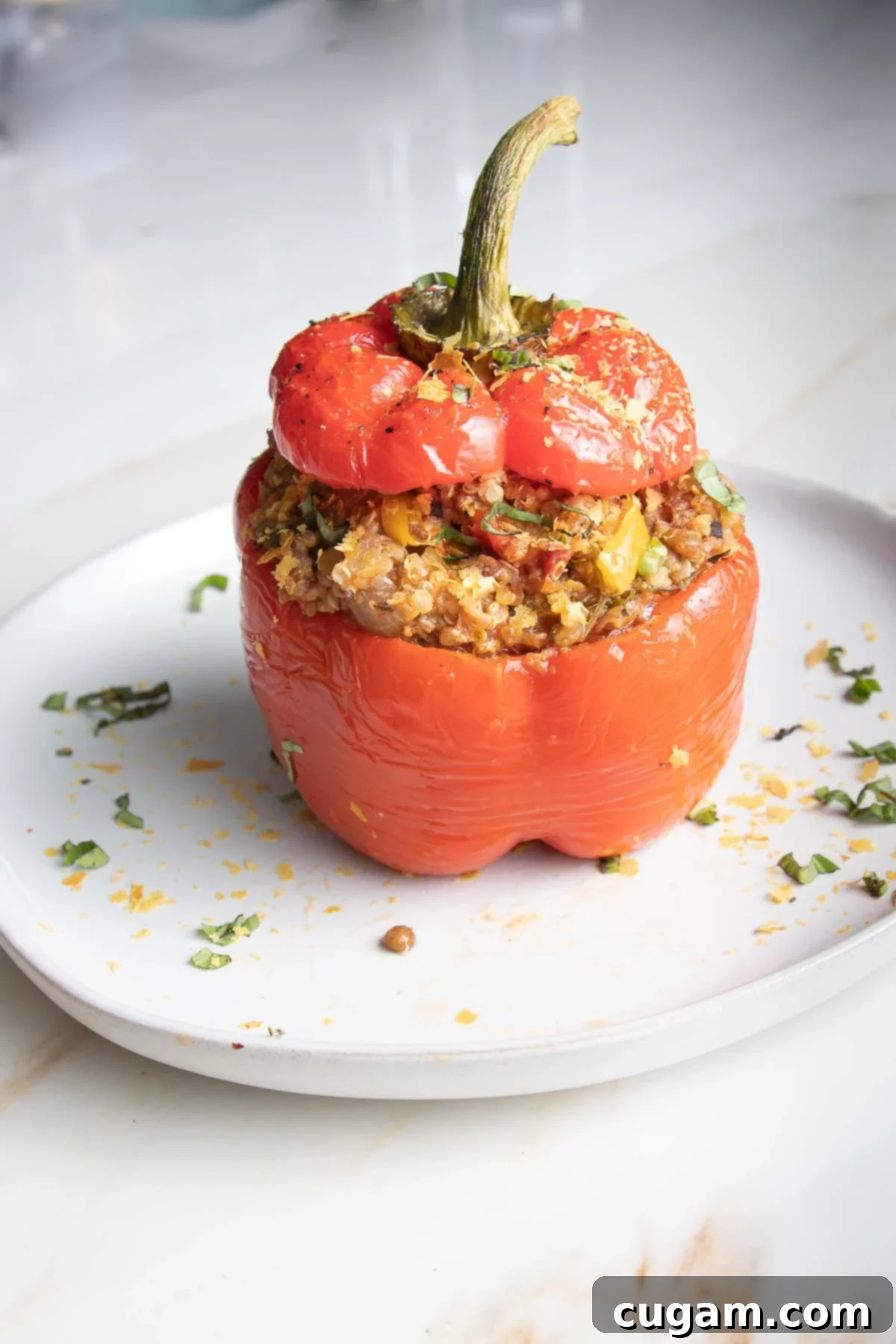 Red bell pepper stuffed with quinoa lentil mixture with the top back on, on a rustic serving board.