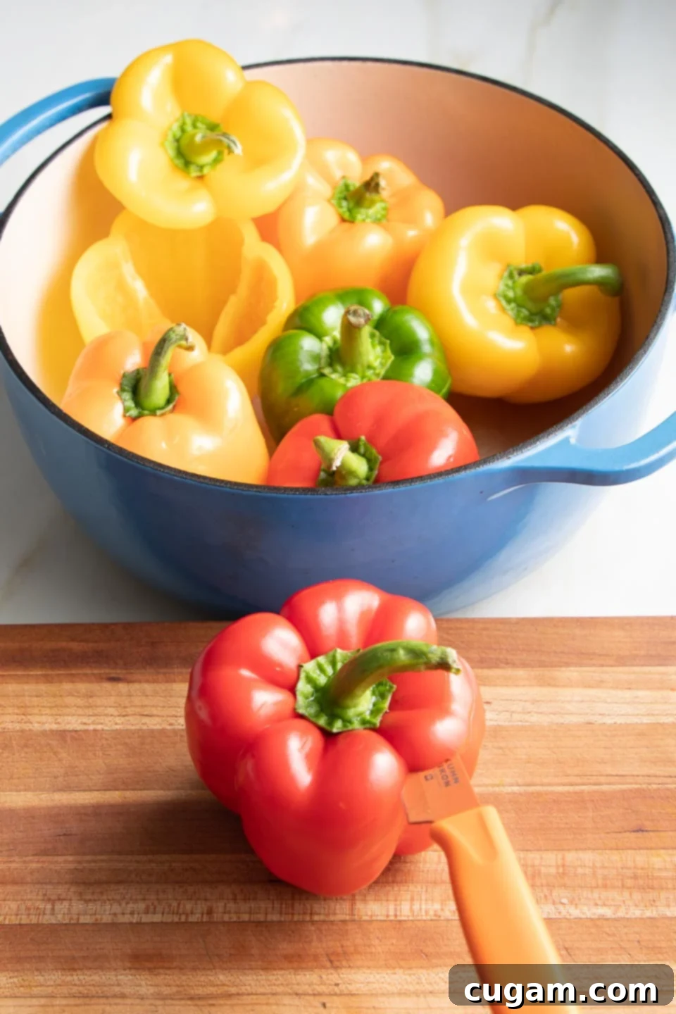 A hand using a sharp knife to slice the top quarter inch off a red bell pepper, preparing it for stuffing.