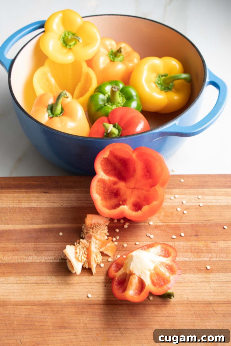 A hand scooping out the seeds and membranes from inside a cut bell pepper using a small paring knife.