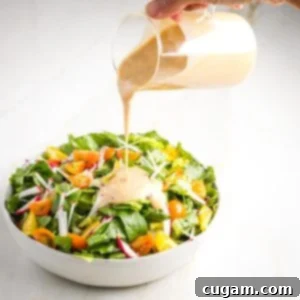 Pouring creamy garlic dressing over a simple, colorful, salad.