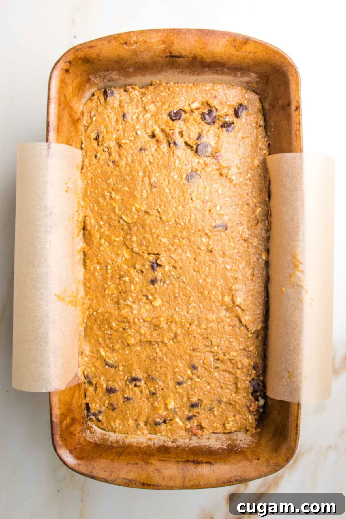 Pumpkin bread batter in a loaf pan lined with parchment
