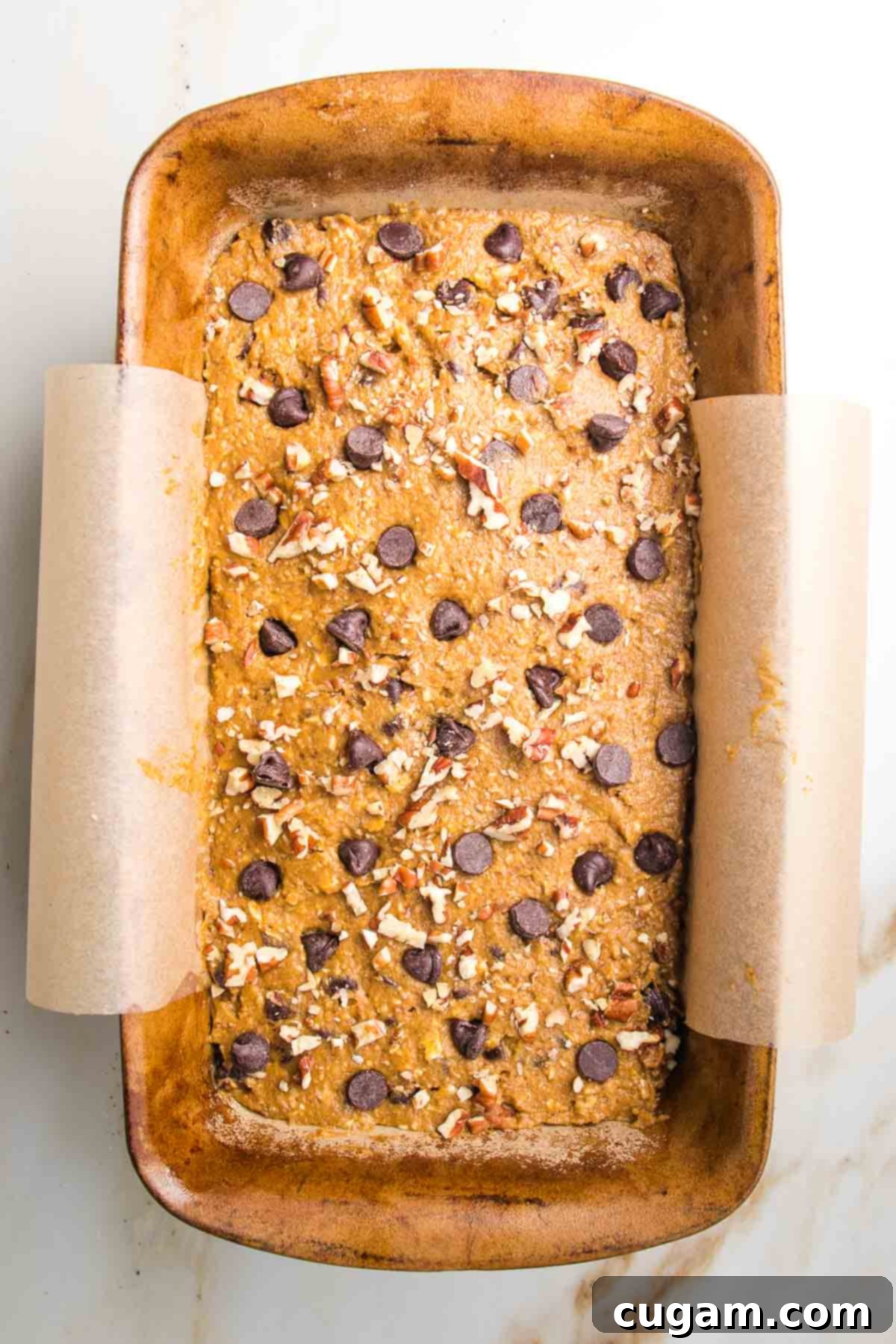 Pumpkin Bread batter in a loaf pan lined with parchment. Sprinkled on top with chocolate chips and chopped pecans.