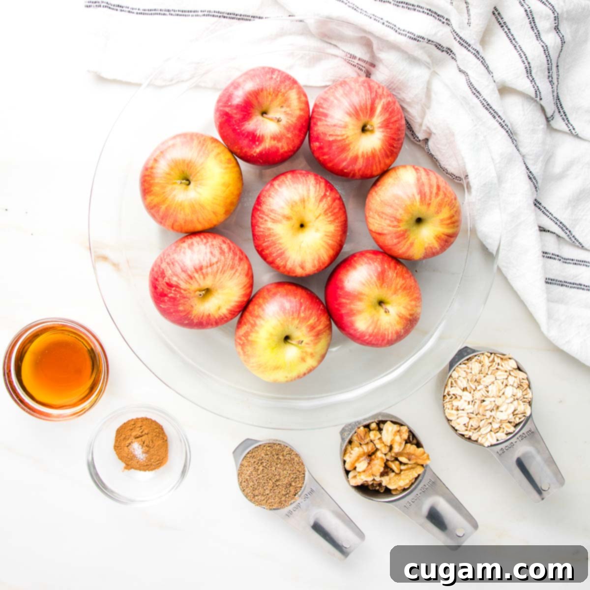 Glass pie plate filled with red apples. Ingredients for baked apples maple syrup, cinnamon, ground flax, walnuts, oatmeal.