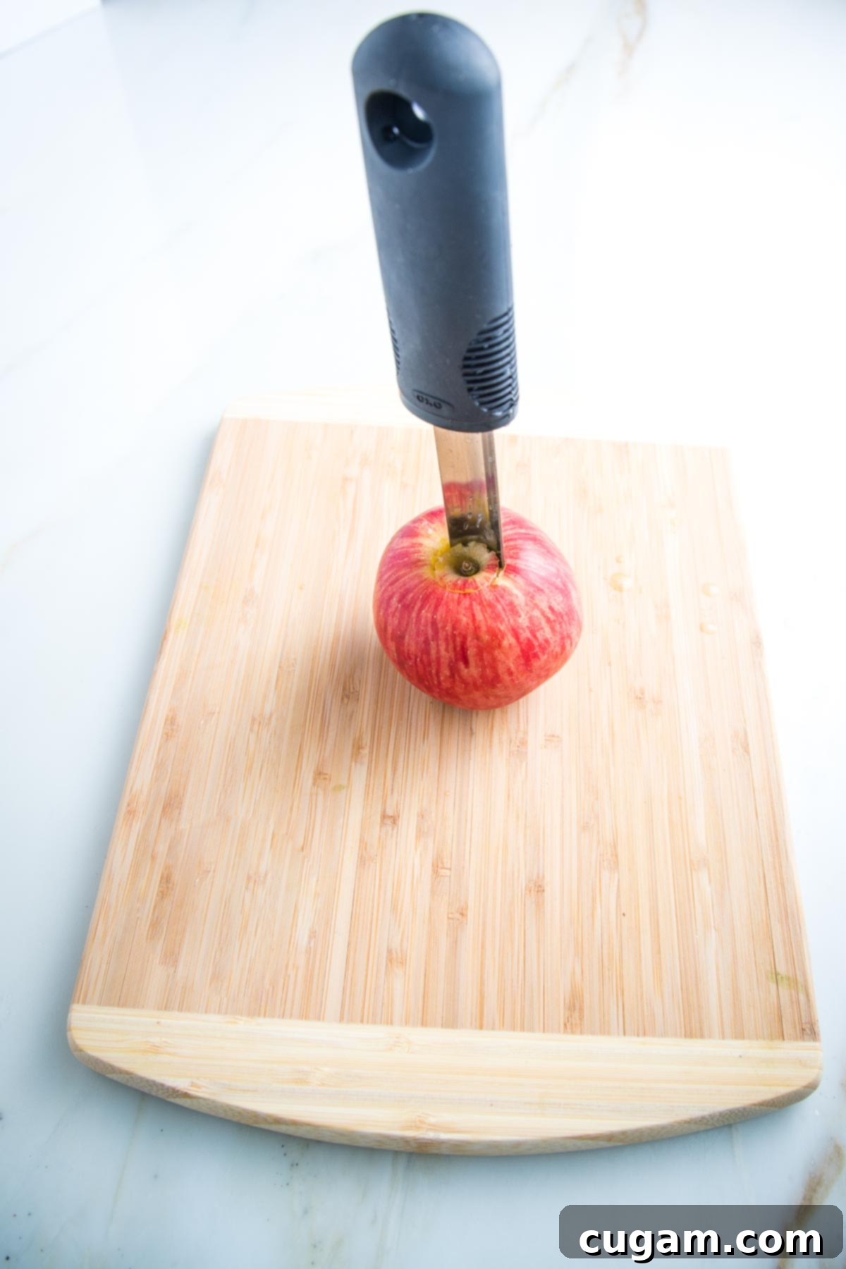 Red apple on a cutting board with an apple corer in the center.