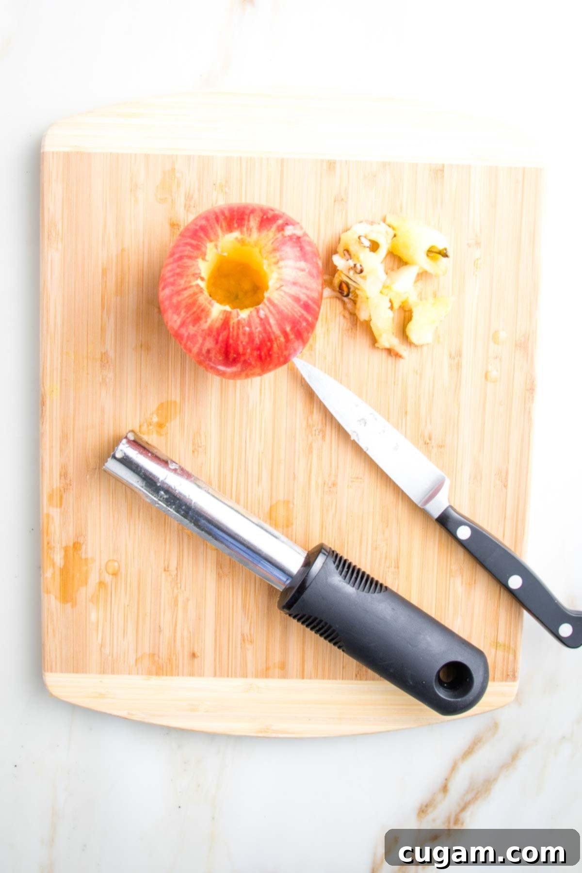 Red apple that's been cored. A paring knife and an apple corer on the cutting board too.