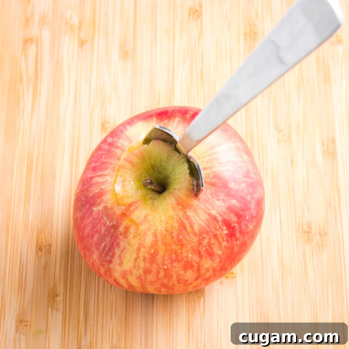 Close up of a red apple on a cutting board with a grapefruit spoon stuck into the center to scoop out the core.