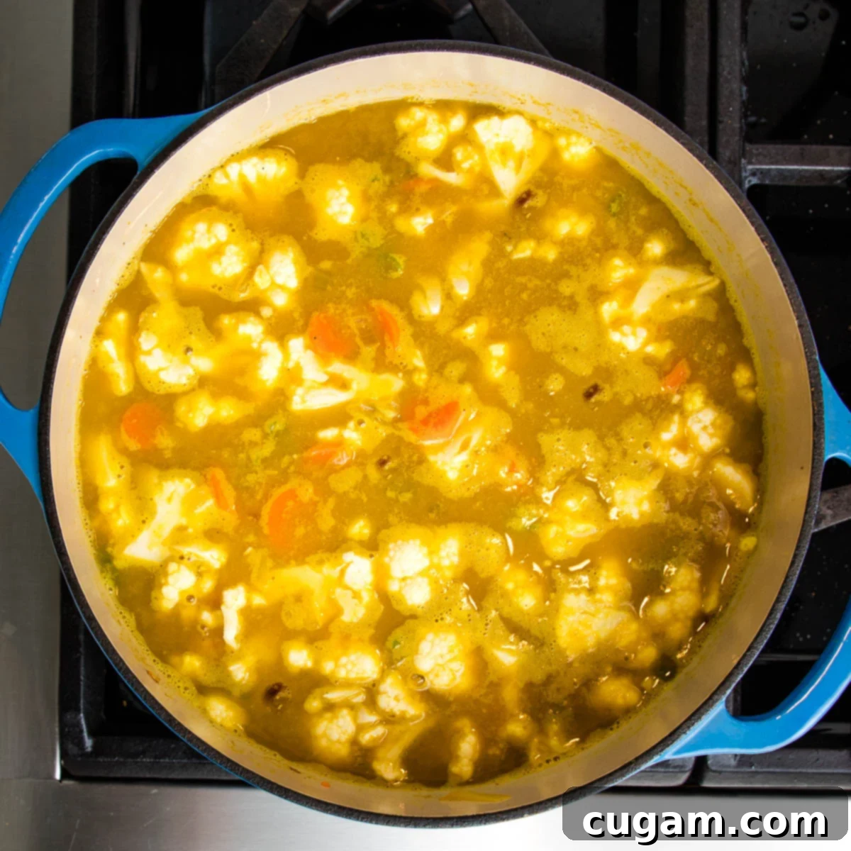 Blue Dutch Oven filled with broth and vegetables, including cauliflower cooking.